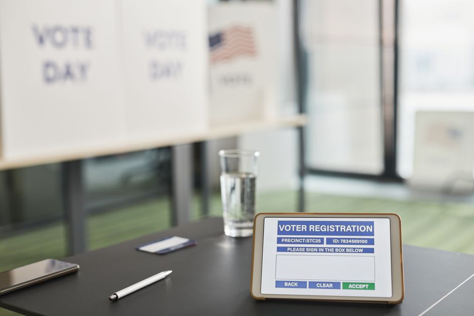 Imagem de uma estação de votação com um tablet exibindo a tela de registro de votação, destacando o processo de participação cívica e eleições.
