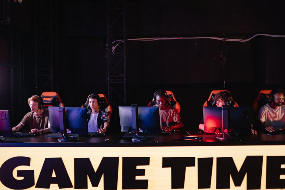 Grupo de jovens jogadores de eSports participando de uma competição de videogame em um ambiente escuro com iluminação de LED.