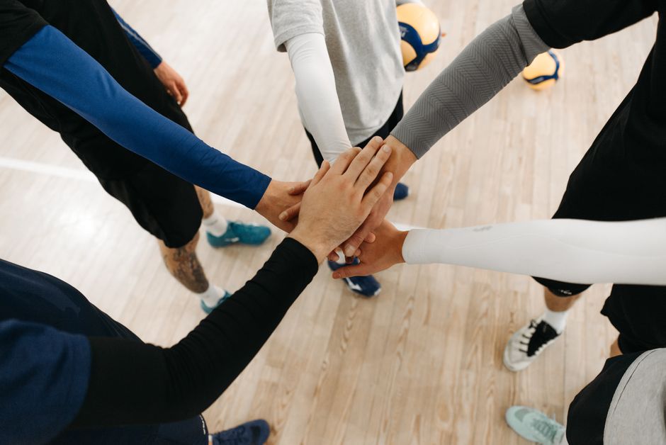 Grupo de pessoas unindo as mãos em sinal de união e colaboração em ambiente esportivo ou de equipe.