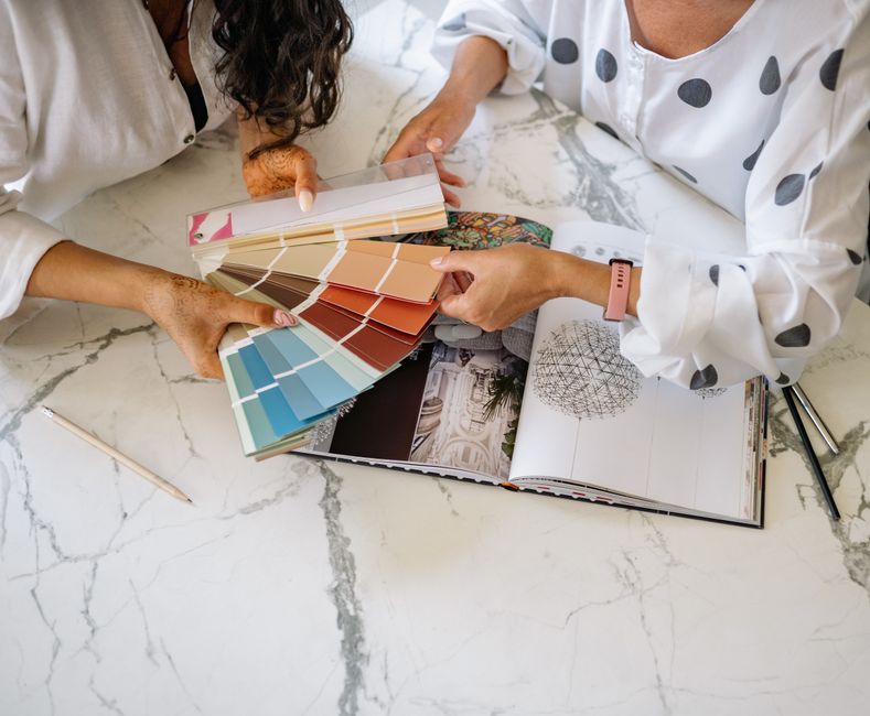 Duas pessoas discutindo e escolhendo cores e projetos para decoração ou design de interiores, focando na seleção de cores e estética.