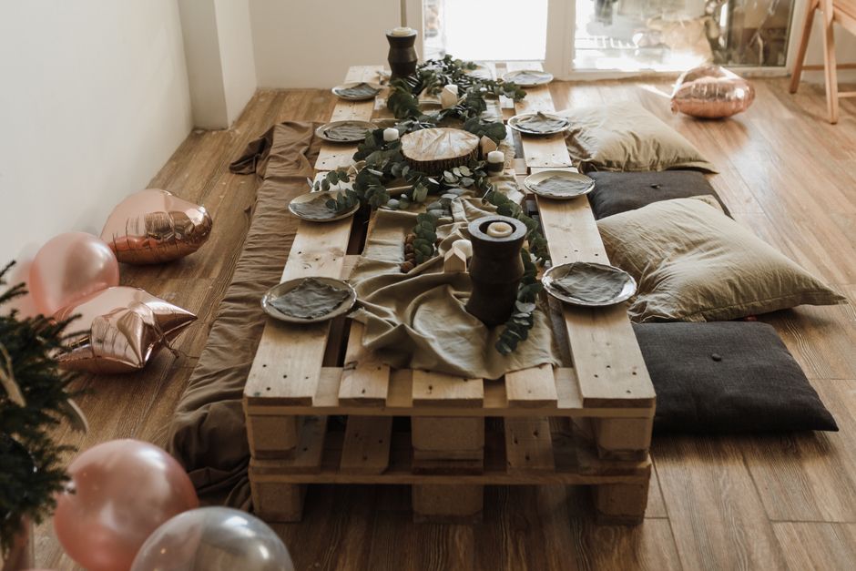 Mesa de jantar decorada de forma rústica com almofadas no chão e balões decorativos ao redor, ideal para uma celebração em um ambiente acolhedor.