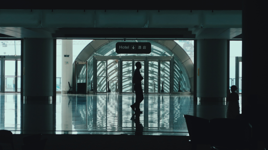 Pessoa caminhando pelo terminal de um aeroporto moderno, com presença de sinalização e estrutura arquitetônica avançada.