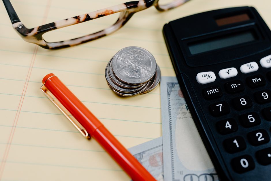 Imagem relacionada à administração financeira, destacando moedas, calculadora e itens de escritório sobre uma mesa.
