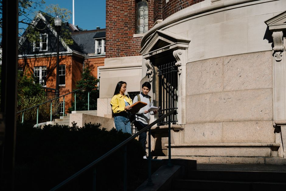 Jovens estudantes estudando e revisando materiais acadêmicos próximos a uma edificação histórica ao ar livre.