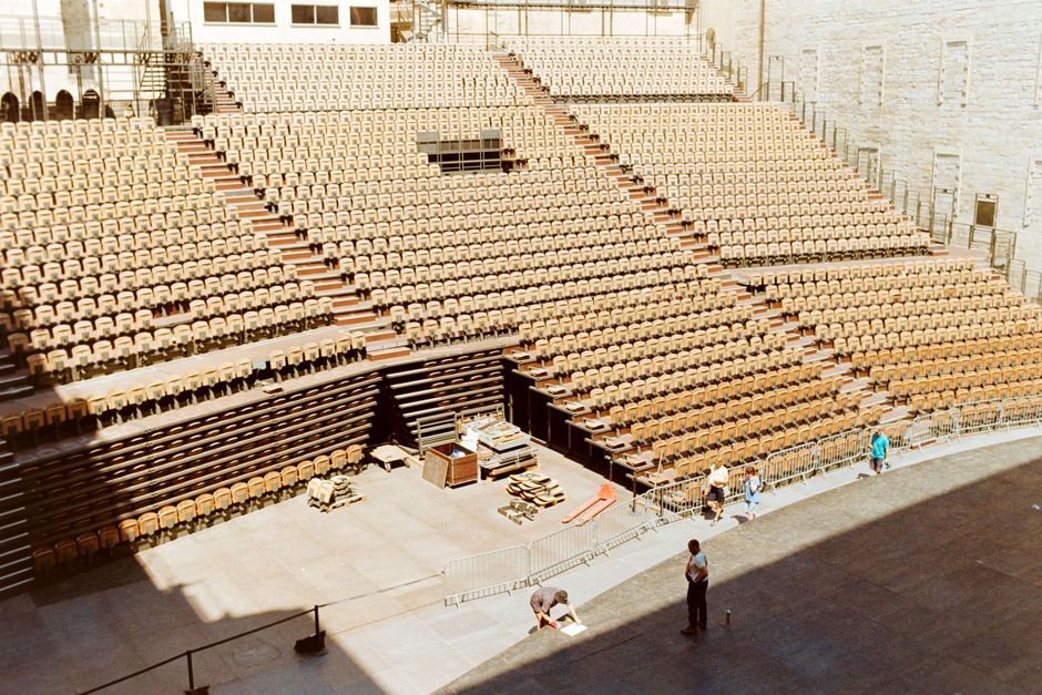 Imagem de um palco de teatro ou grande auditório vazio, com assentos organizados em filas, preparado para um evento ou ensaio.