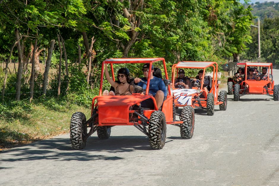 Grupo de pessoas desfrutando de um passeio em carrinhos off-road ao ar livre, com árvores verdes ao fundo.