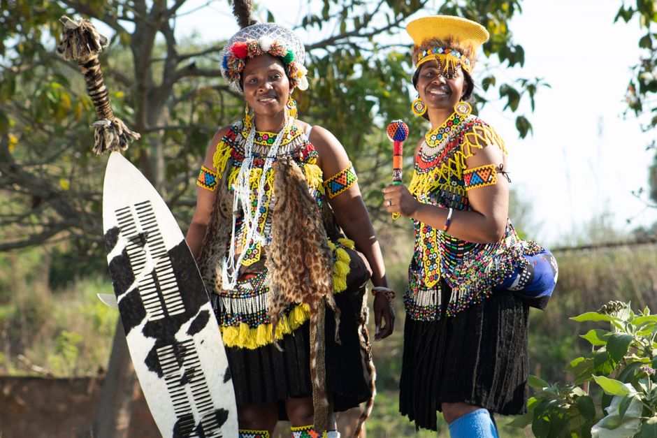 Mulheres de etnia africana vestidas com trajes tradicionais, participando de uma celebração cultural ao ar livre.