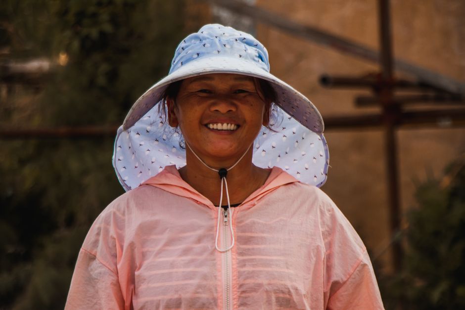 Mulher sorridente usando chapéu de proteção solar em ambiente ao ar livre, transmitindo bem-estar e conexão com a natureza.