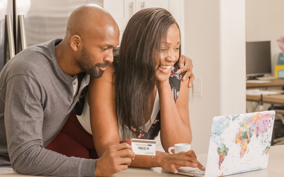Casal feliz fazendo compras online com um laptop, simbolizando planejamento financeiro ou compras pela internet.