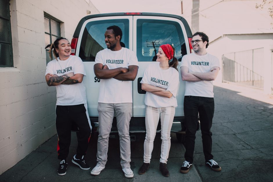 Grupo de voluntários sorridentes em frente a uma van, representando trabalho em equipe e solidariedade social.