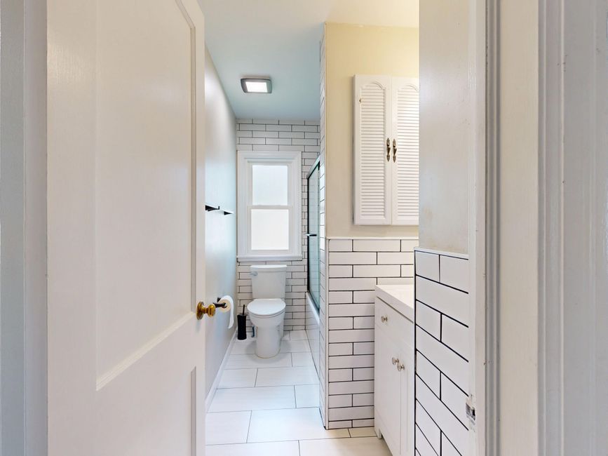 Banheiro compacto e bem iluminado com acabamento em azulejos brancos e móveis brancos, ideal para decoração moderna e funcional.