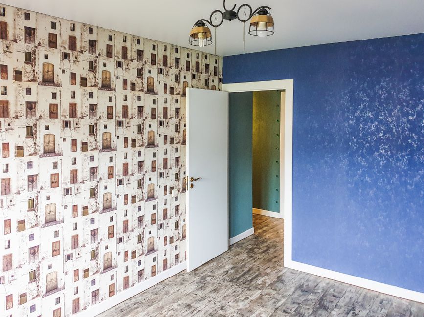 Imagem de um ambiente interno com paredes decoradas de forma moderna, uma das paredes com papel de parede com padrão de janelas e a outra pintada de azul, iluminação de teto com luminária moderna, ideal para artigos sobre arquitetura de interiores ou decoração de ambientes.