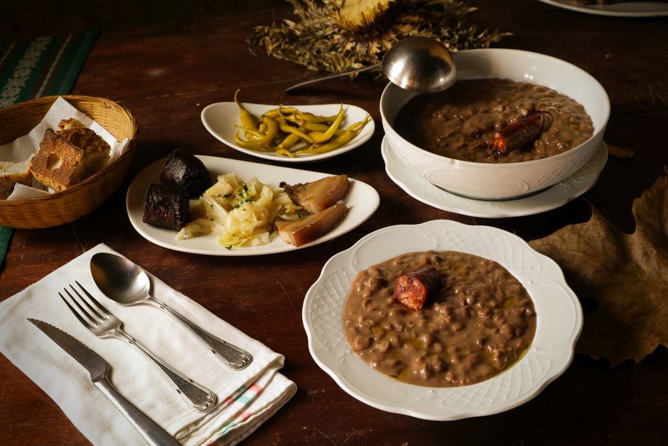 Mesa rústica com pratos típicos de feijoada, incluindo feijão preto, acompanhamentos e pimentas, em ambiente acolhedor.