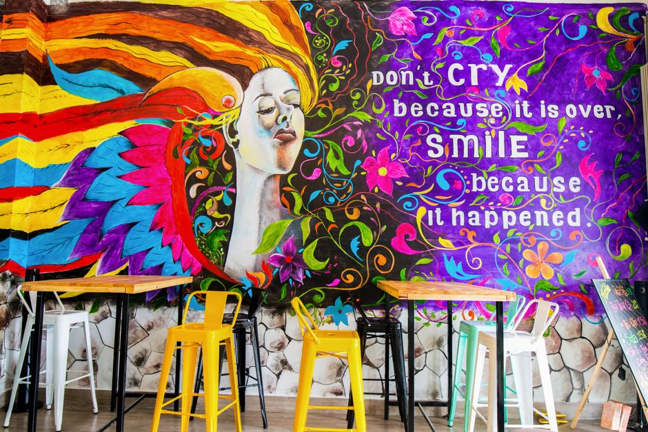 Mural colorido com mensagem inspiradora em um ambiente modernoconfessionista, com mesas e cadeiras em cores variadas para um espaço criativo e acolhedor.