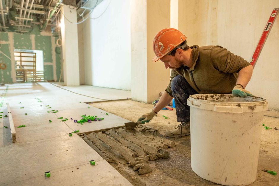 Profissional aplicando argamassa em uma obra de construção civil, com foco na preparação do piso.