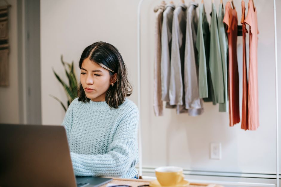 Mulher trabalhando de casa com roupas organizadas ao fundo, transmitindo o tema de empreendedorismo e produtividade no home office.