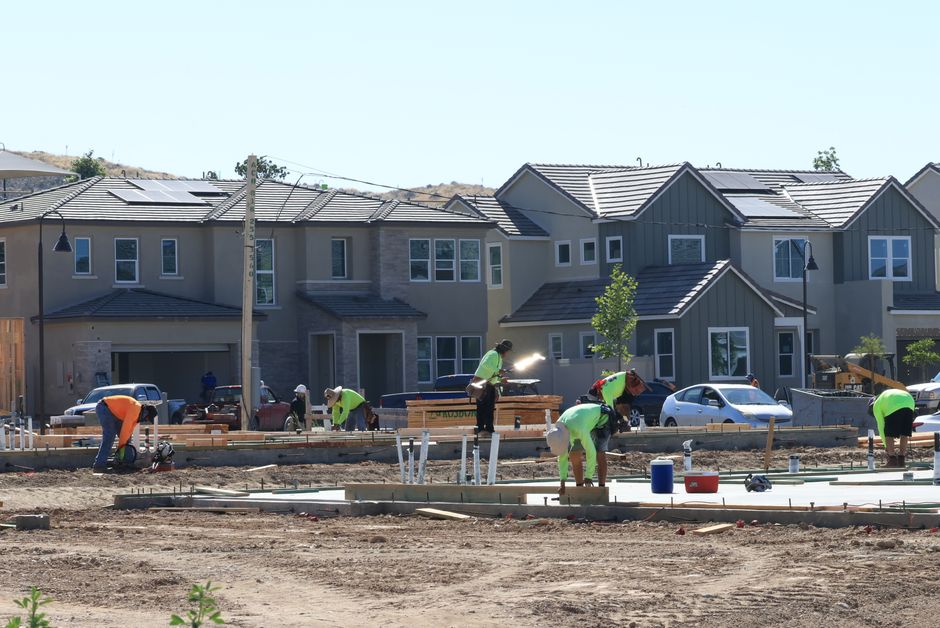 Construção de casas em um bairro residencial em andamento, com trabalhadores realizando tarefas no terreno.