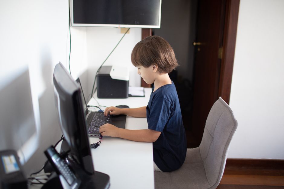 Garoto utilizando um computador e uma televisão em um ambiente doméstico, simbolizando o ensino a distância ou o aprendizado online para blogs de educação ou tecnologia.