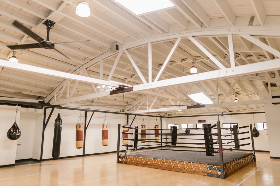 Imagem de uma academia de boxe com ringue e equipamentos de treinamento para prática de esportes de combate.