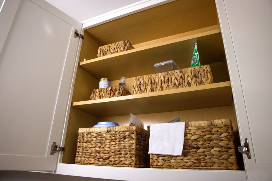 Fotografia de um armário aberto com cestas de armazenamento de vime organizando itens diversos em uma cozinha moderna.