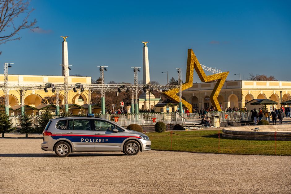 Imagem de um parque ou praça decorada para o Natal com uma estrela gigante de decoração, uma viatura policial alemã e turistas explorando o local, ideal para artigos sobre segurança e festividades natalinas.
