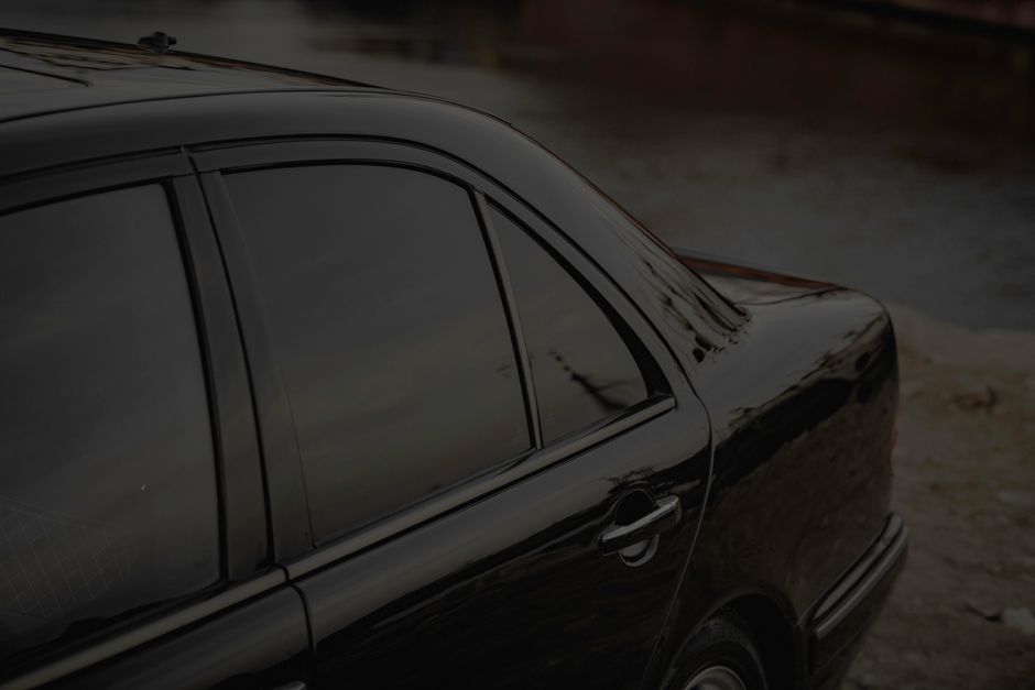 Imagem de um carro preto estacionado ao lado de uma estrada, com ênfase no veículo e seu acabamento brilhante.