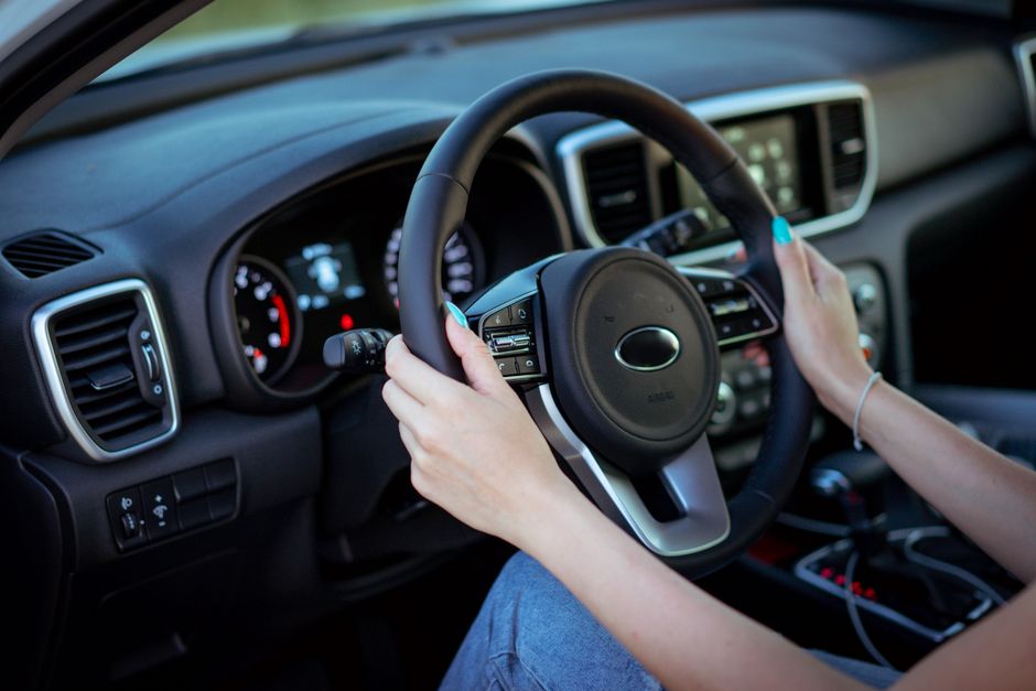 Imagem de uma pessoa segurando o volante de um carro, simbolizando direção, controle e mobilidade.