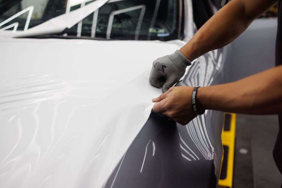 Pessoa aplicando filme de proteção em carro para melhorar estética e proteger a pintura.