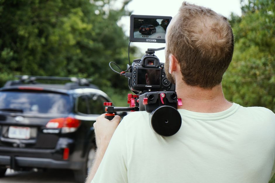 Fotógrafo capturando vídeos de veículos em movimento ao ar livre, destacando a produção de conteúdo audiovisual para o setor automobilístico.