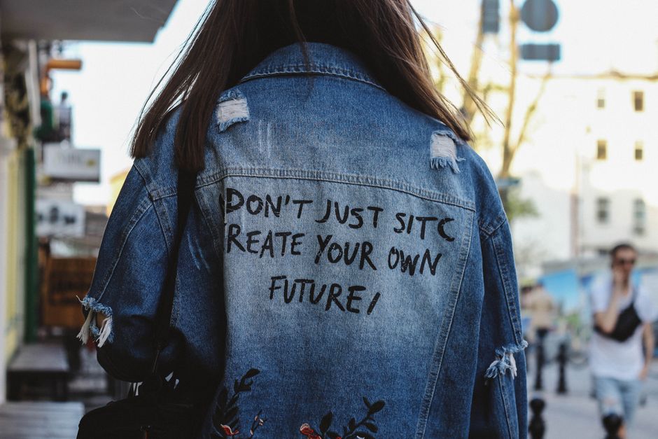 Pessoa usando jaqueta jeans com mensagem inspiradora na rua, transmitindo uma ideia de autonomia e empoderamento.