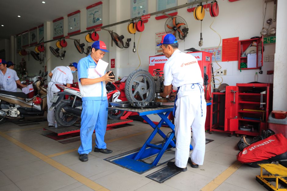 Técnicos de oficina técnica realizando manutenção de motocicletas em uma oficina especializada, focando em inspeção e reparo de componentes mecânicos.