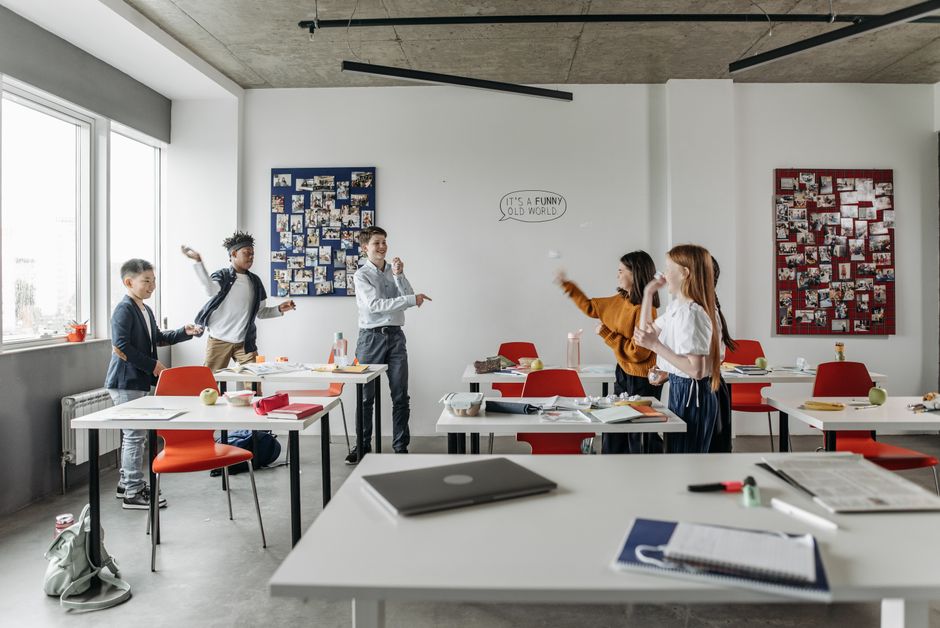 Imagem de crianças brincando e interagindo em uma sala de aula moderna, com ambientes abertos e decoração colorida.