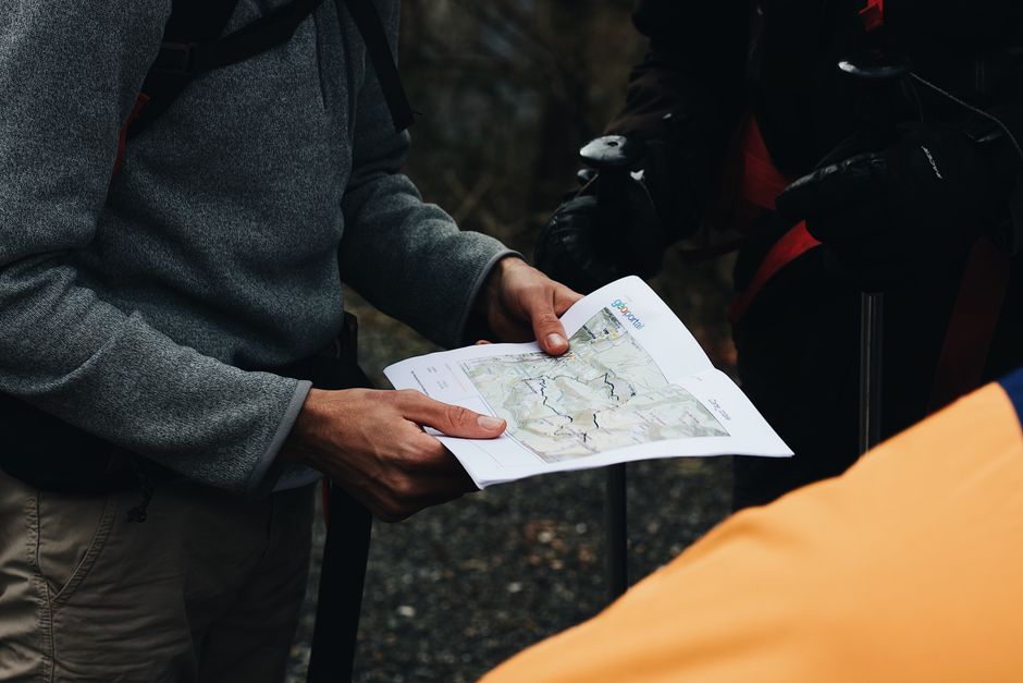 Pessoas analisando um mapa ao ar livre, simbolizando planejamento de viagens ou aventuras na natureza.