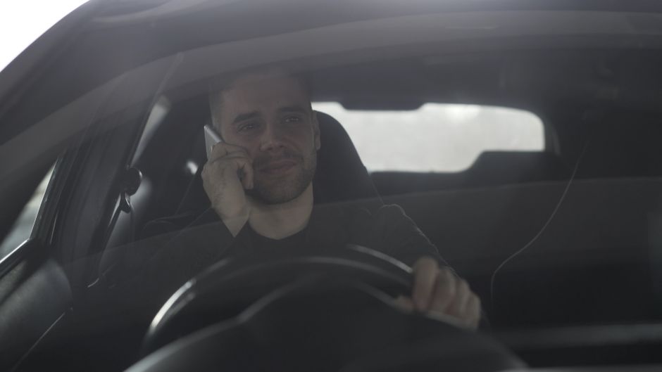 Homem dirigindo e falando ao telefone dentro de um carro, possivelmente durante uma viagem ou deslocamento.