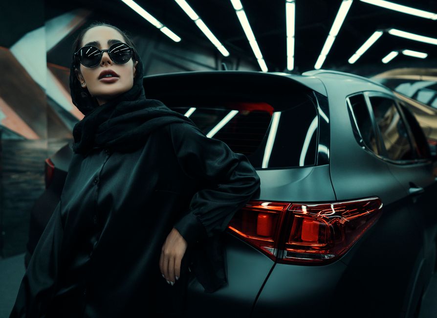 Mulher estilosa posando ao lado de carro em ambiente moderno, transmitindo uma imagem de luxo e moda.