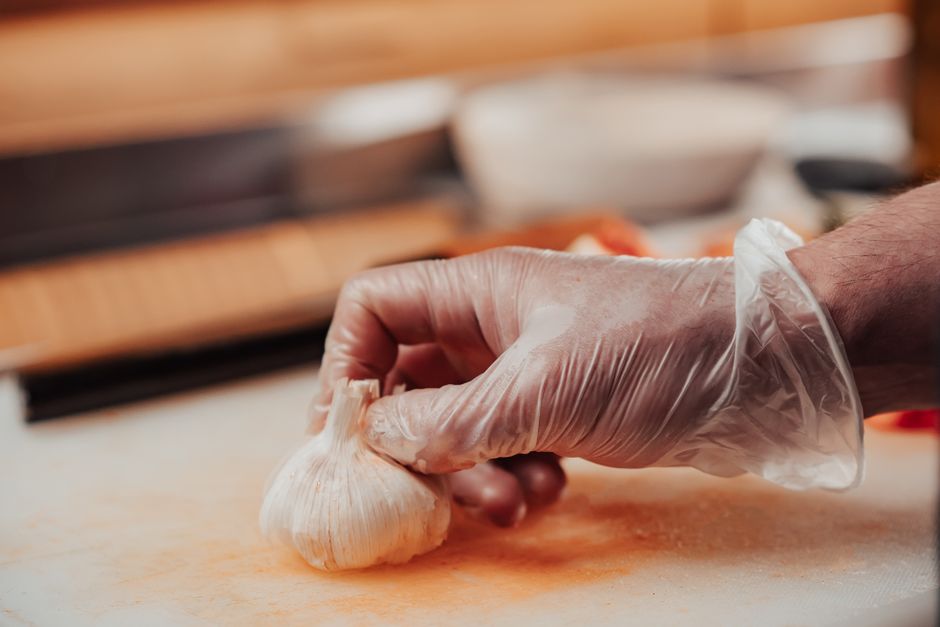 Pessoa preparando alho em um ambiente de cozinha, usando luvas de plástico para higiene.