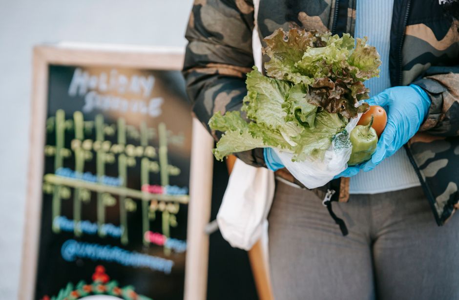 Pessoa segurando um saco de verduras orgânicas em um mercado ou feira, destacando o consumo consciente e produtos naturais.
