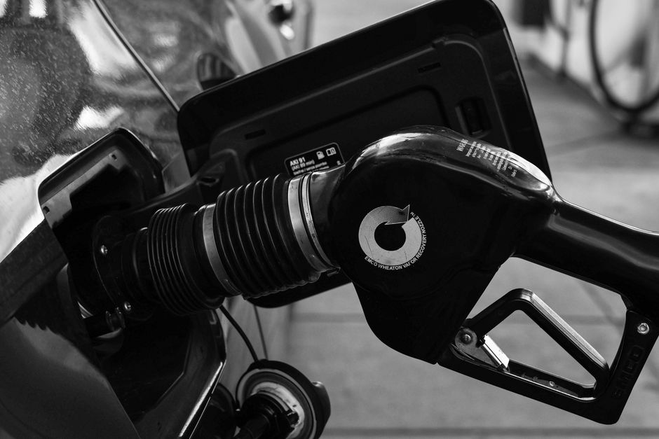 Imagem de um posto de gasolina com um recipiente de combustível conectado a um veículo, destacando o tema de abastecimento e transporte de combustíveis.
