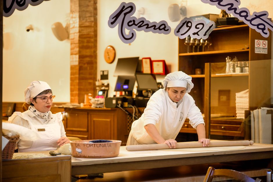 Duas padeiras preparadas em uma padaria artesanal, demonstrando o processo de fabricação de pão.