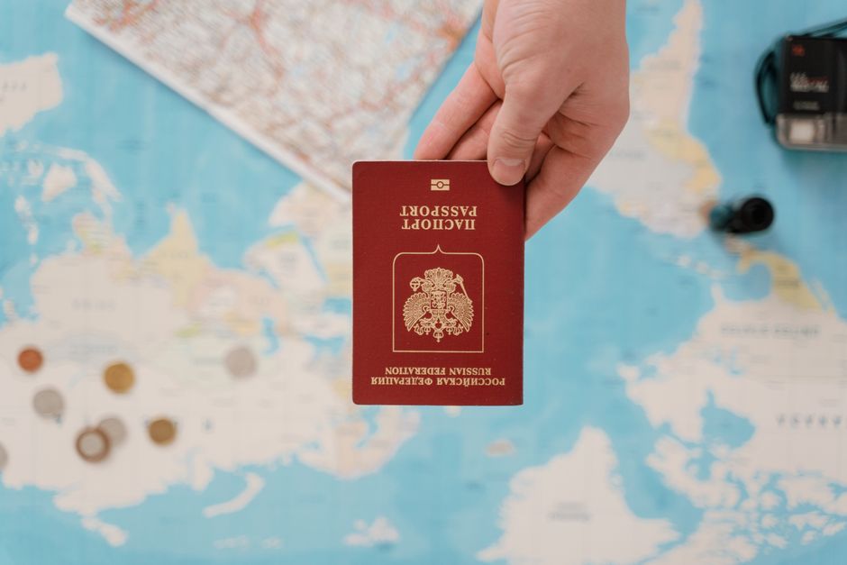 Imagem de uma pessoa segurando um passaporte diplomático diante de um mapa mundial, representando temas de viagens internacionais e documentação oficial.