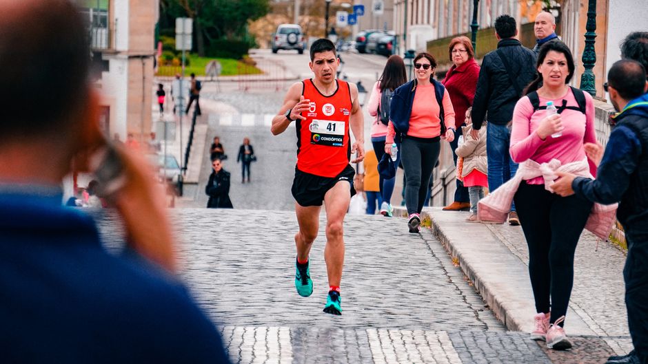 Corredor participando de uma prova de corrida em rua urbana, cercado por espectadores e apoiadores.
