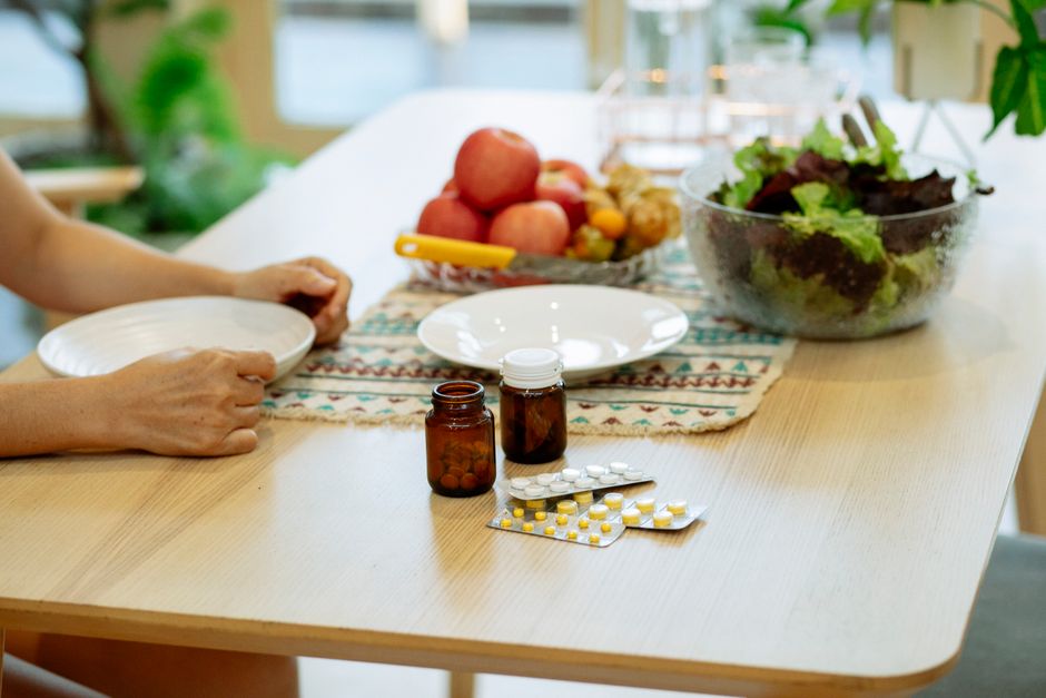 Pessoas em um ambiente doméstico preparando uma refeição saudável com frutas, salada e remédios, em um contexto de cuidados com saúde e bem-estar.