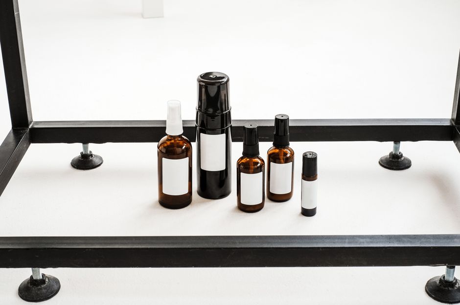 Imagem de diferentes frascos de produtos naturais, possivelmente essenciais ou de cuidados pessoais, organizados sobre uma superfície branca com suporte metálico.