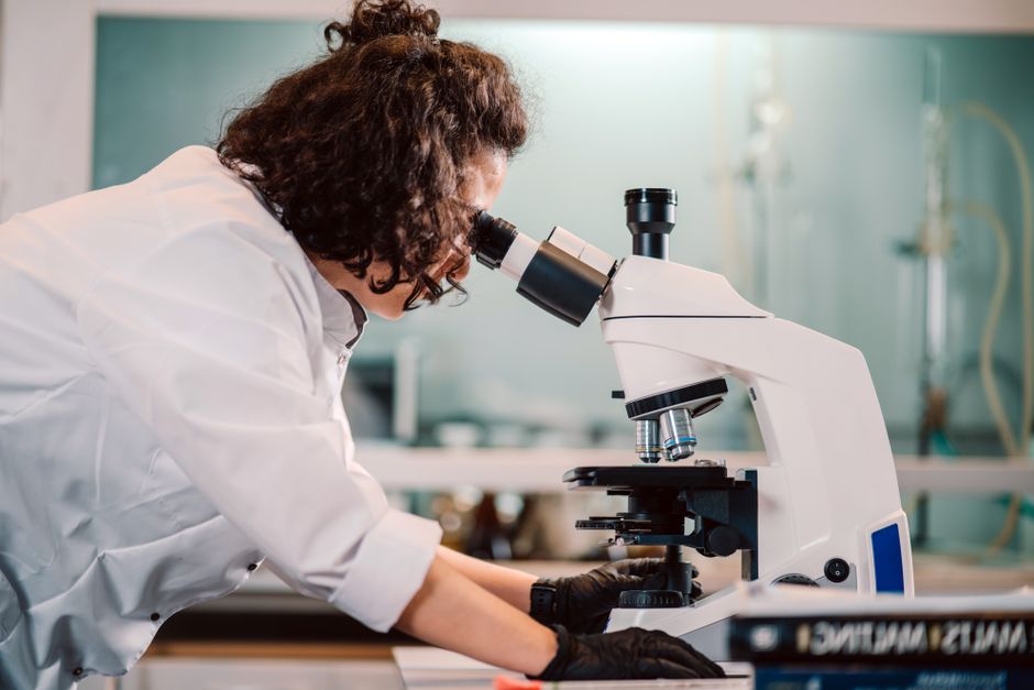 Cientista observando uma amostra através de um microscópio em um laboratório de pesquisa.