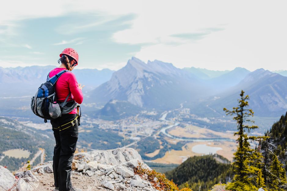 Imagem de uma pessoa de mochila e capacete em uma trilha de montanha, simbolizando aventura e contato com a natureza.