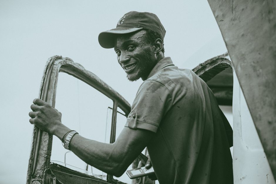 Homem sorridente e informal brincando com uma estrutura metálica ao ar livre, transmitindo uma sensação de descontração e alegria na fotografia.