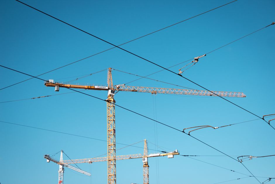 Imagem de torres de canteiro de obras com guindastes contra um céu azul, simbolizando construção e desenvolvimento urbano.