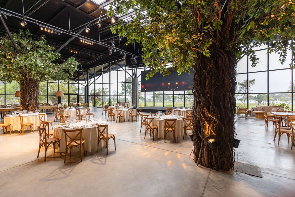 Salão de eventos futurista com grandes árvores integradas ao espaço, criando uma atmosfera única e sustentável para celebrações ao ar livre.