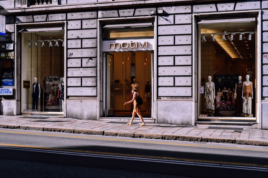 Imagem de uma fachada de loja de roupas na cidade, com uma pessoa caminhando na calçada em frente à vitrine.