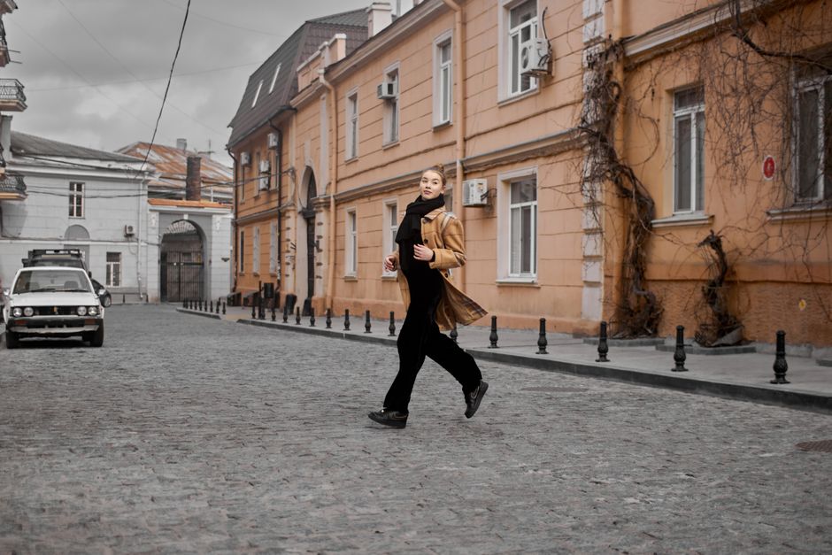Mulher atravessando a rua de cabeça erguida em um cenário urbano com edifícios históricos, demonstrando liberdade e confiança na cidade.